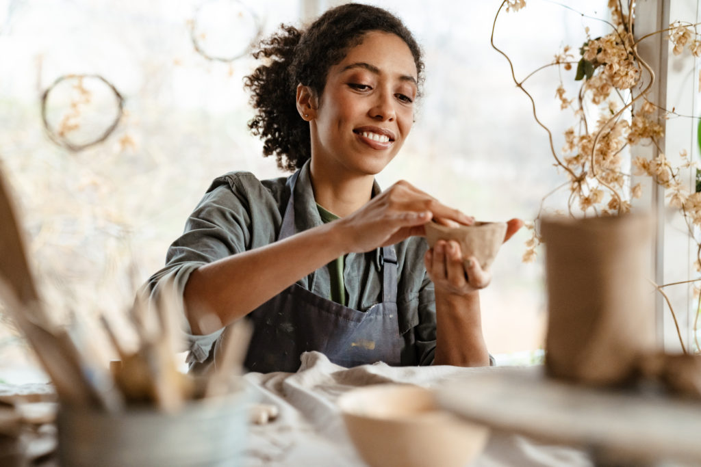 Young black ceramist woman wearing apron sculpting in clay at her workshop