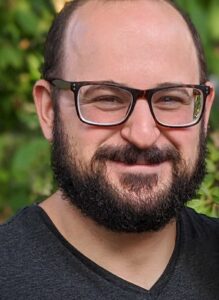 ML Ops Engineer III Ethan, smiling outdoors with glasses and a beard